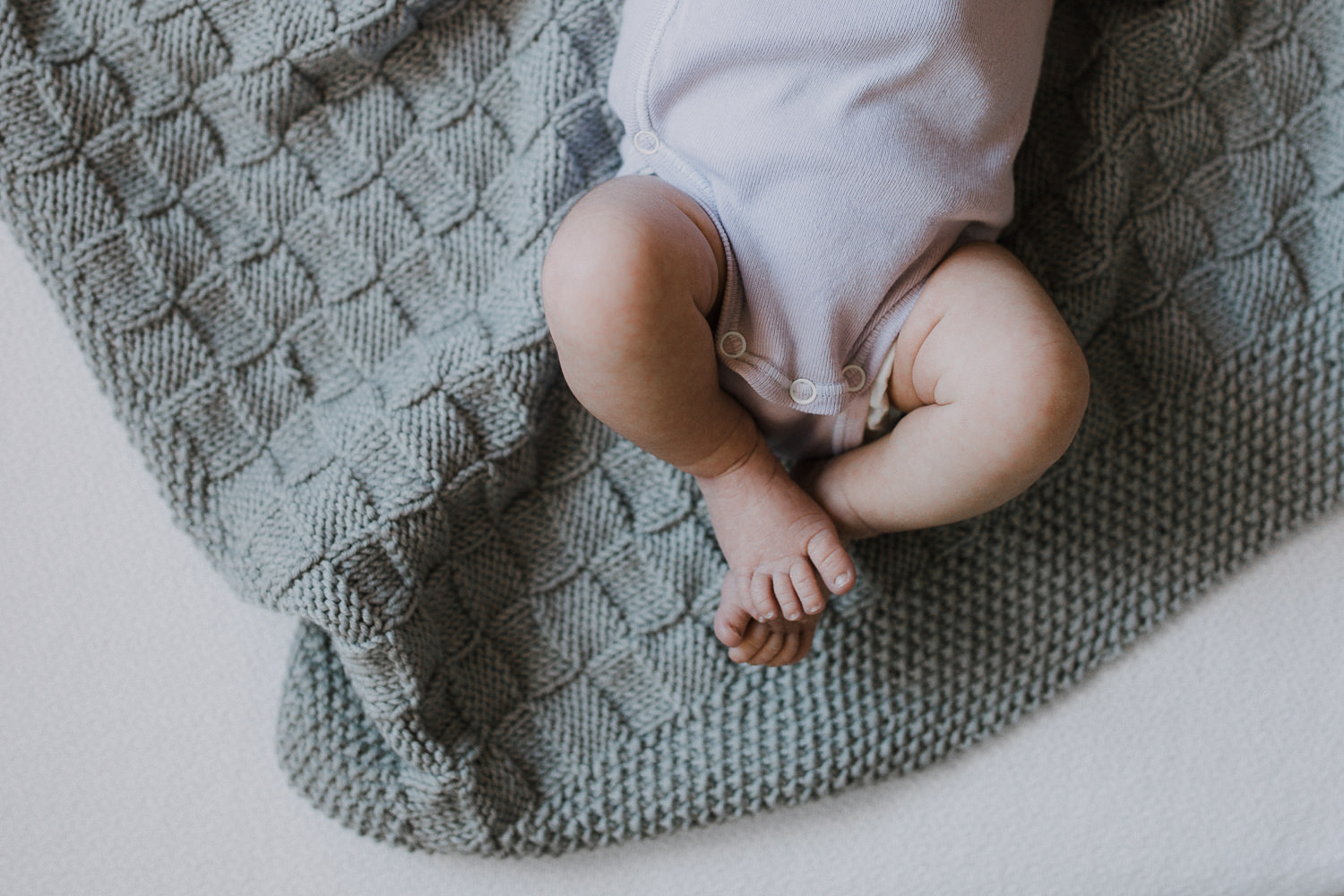 2 week old baby girl in purple onesie lying on hand knitted grey blanket. close up of feet - Newmarket In-Home Photos