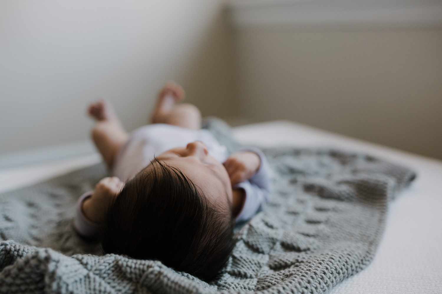 2 week old baby girl with dark hair lying on hand knitted grey blanket - Barrie In-Home Photos