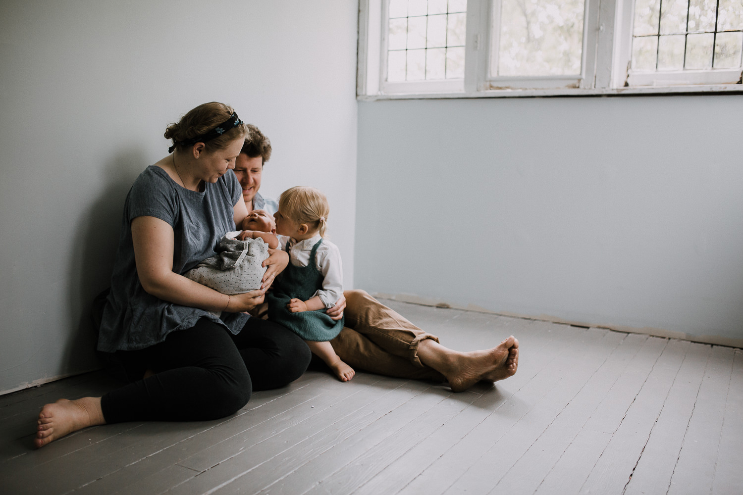 family of four sitting on floor, toddler sister looking at baby brother in mom's arms - Newmarket Lifestyle Family Photography