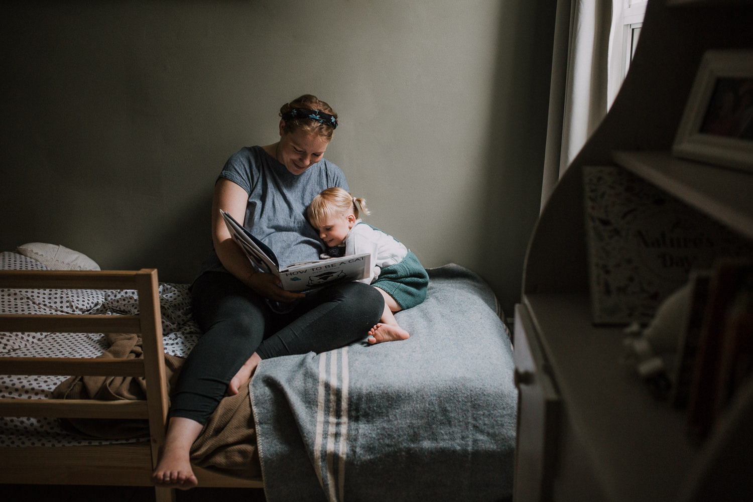 2 year old toddler girl sits on bed with mom, giving her a kiss on the cheek - Newmarket Lifestyle Family Photos