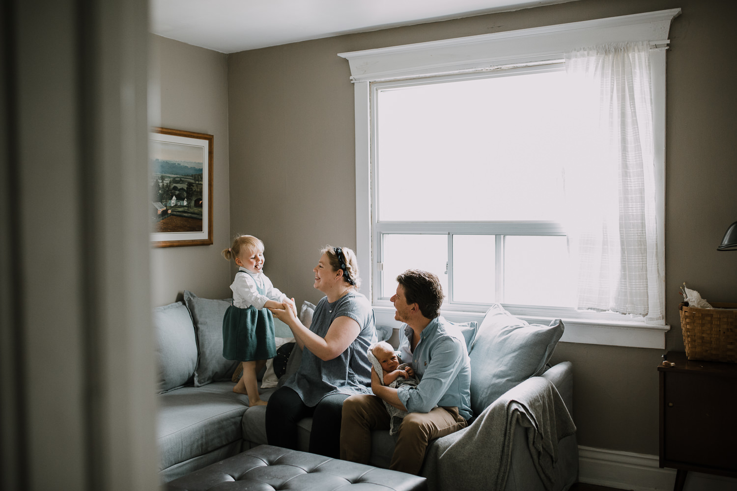 family of four on couch, dad hold 10 day old baby boy while 2 year old toddler girl stands on couch - Stouffville Lifestyle Family Photos