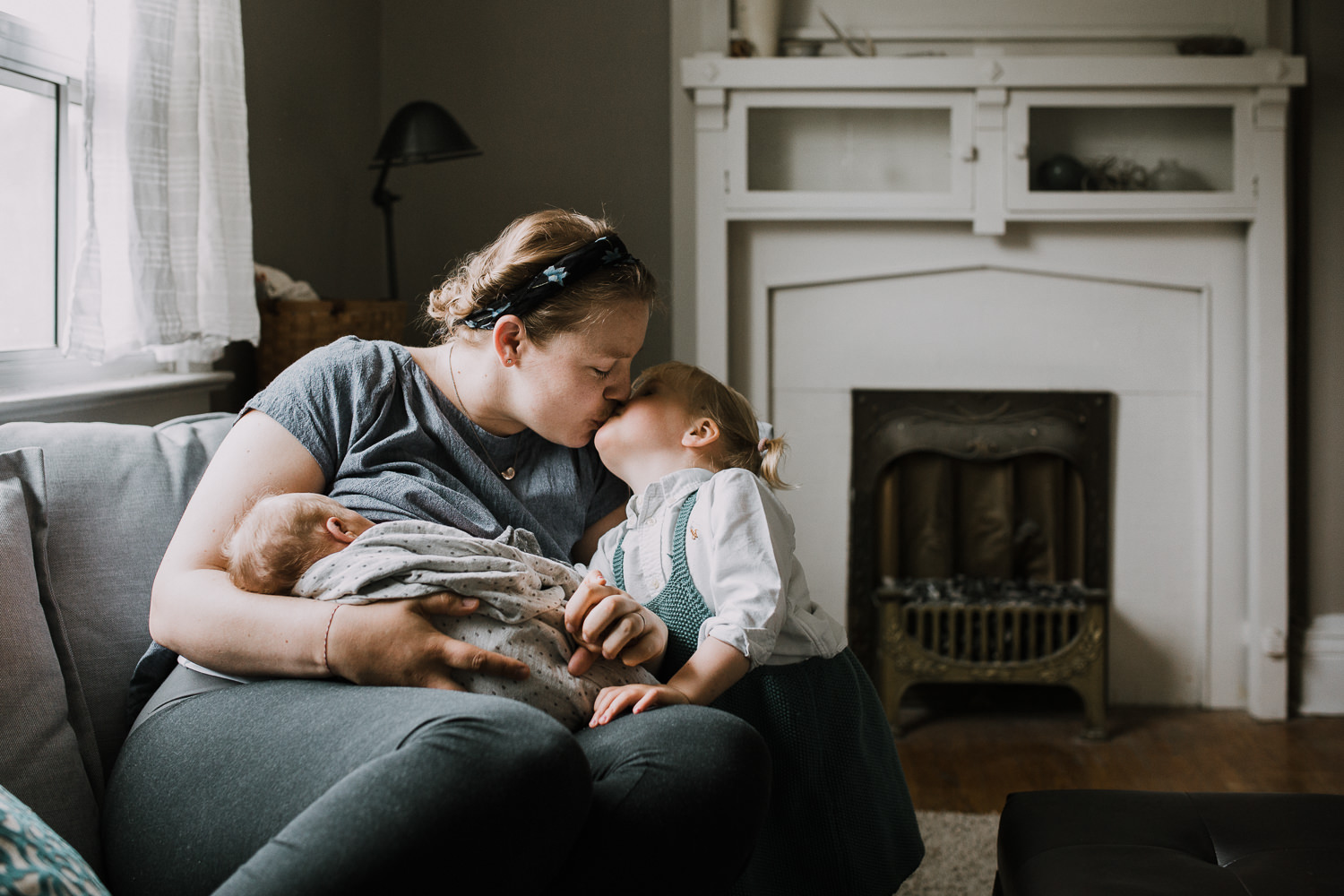 mother sits on couch breastfeeding 10 day old baby boy and kissing 2 year old daughter - Barrie In-Home Family Photography