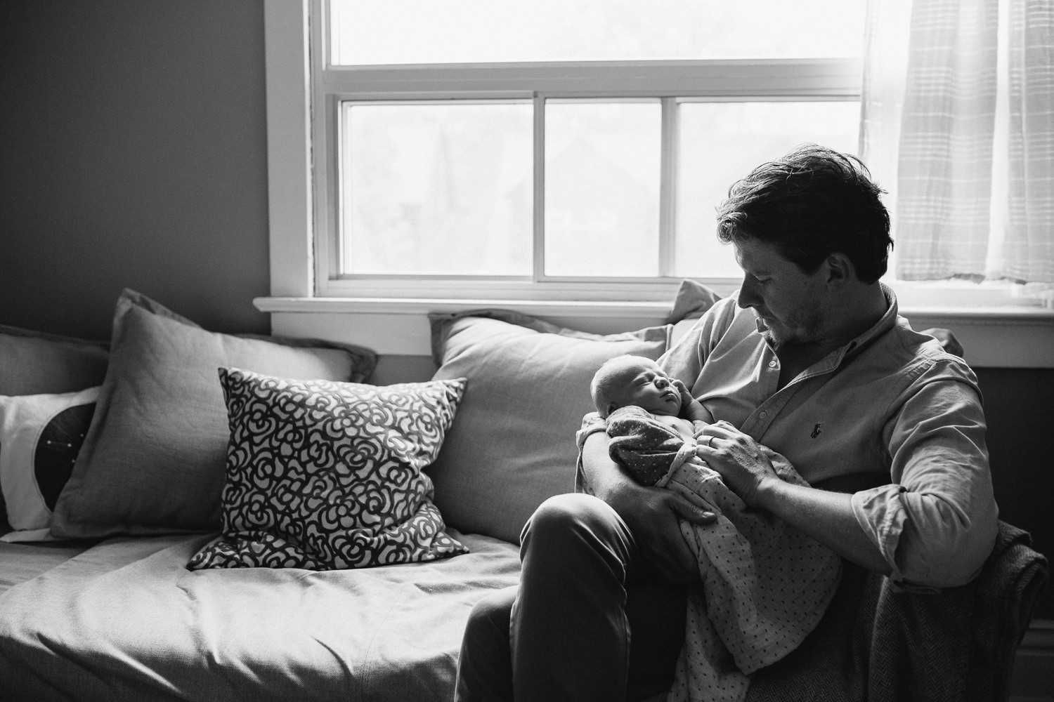 father sits on couch holding sleeping 10 day old baby boy - Markham Lifestyle Family Photos