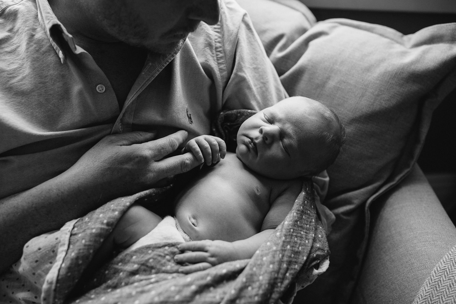 father sits on couch holding sleeping 10 day old baby boy - Barrie Lifestyle Family Photos