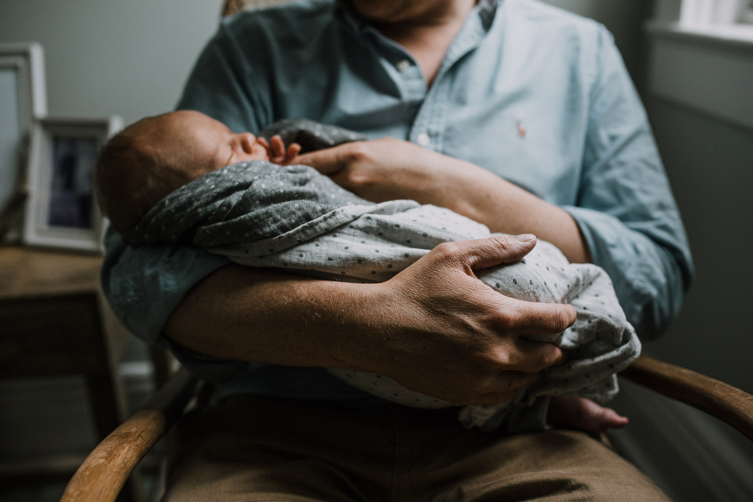 father sits in nursery rocking chair holding sleeping 10 day old baby boy - Newmarket Lifestyle Family Photography