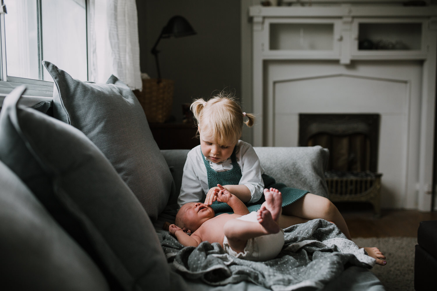 2 year old toddler girl sitting on couch looking at and soothing 10 day old baby brother - Newmarket In-Home Family Photos
