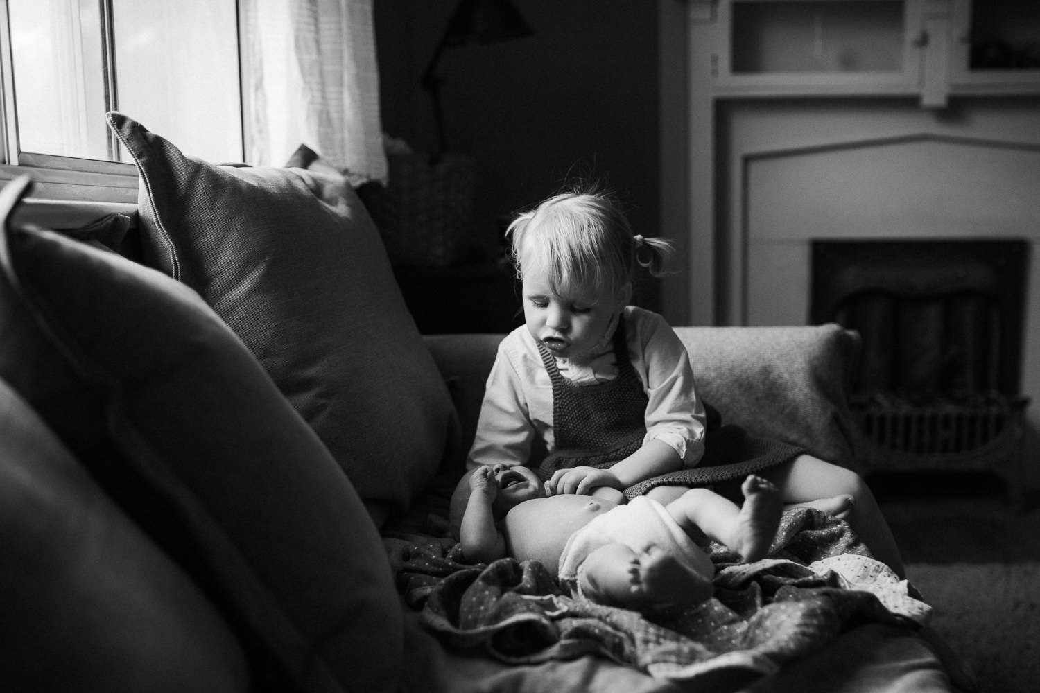 2 year old toddler girl sitting on couch looking at and soothing 10 day old baby brother - Stouffville In-Home Family Photos