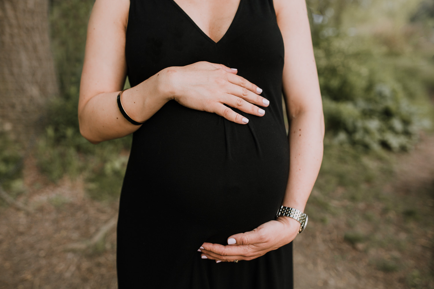 pregnant woman in black dress standing with arms around baby bump - Newmarket Lifestyle Photography