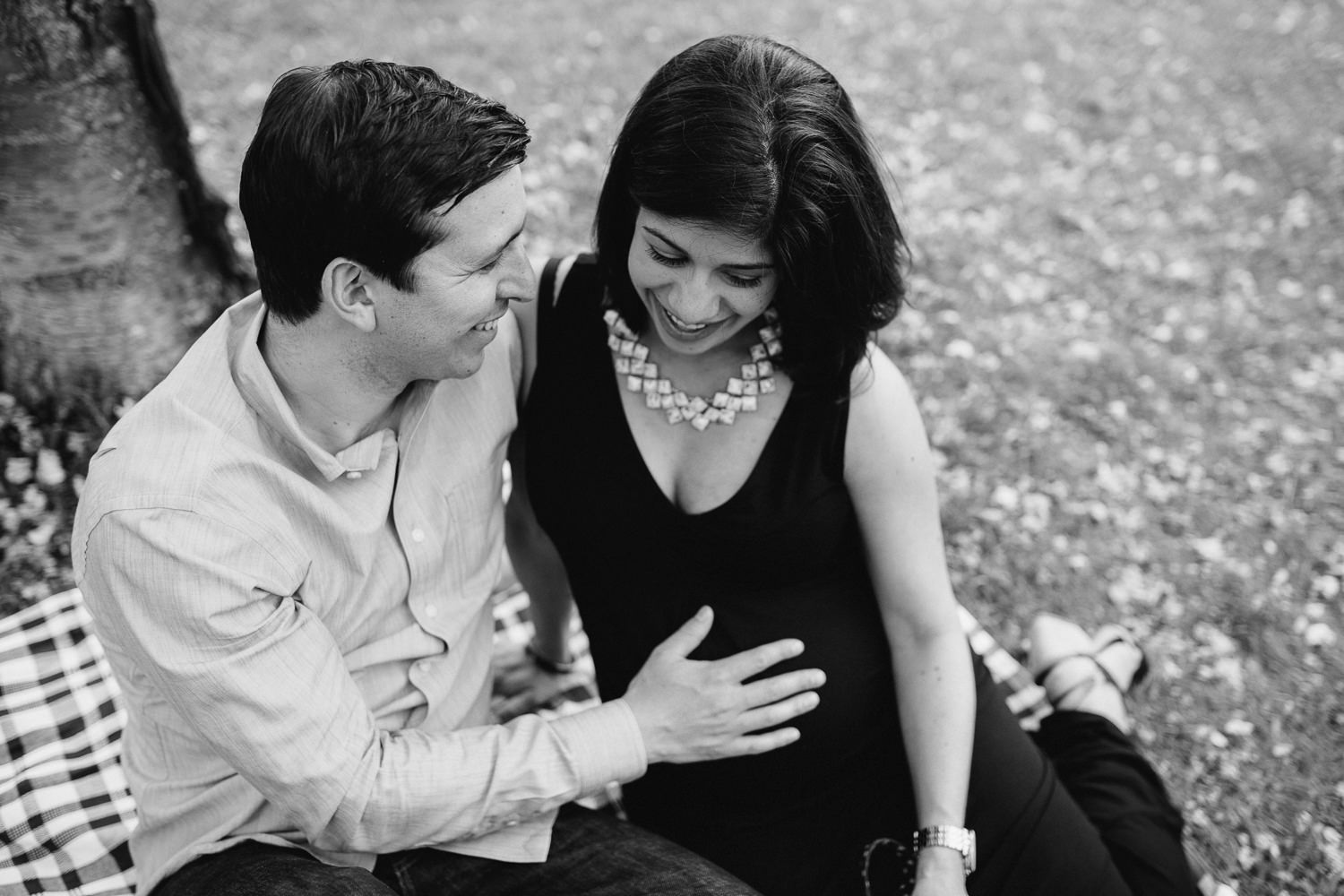 husband and pregnant wife sitting on a blanket in the park, his hand on her baby bump - Stouffville Lifestyle Photos