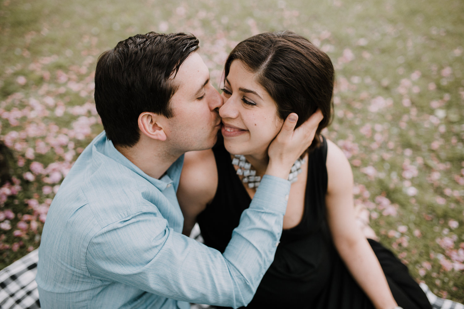 husband and pregnant wife sitting on a blanket in the park, man kissing woman on cheek - Markham Lifestyle Photos