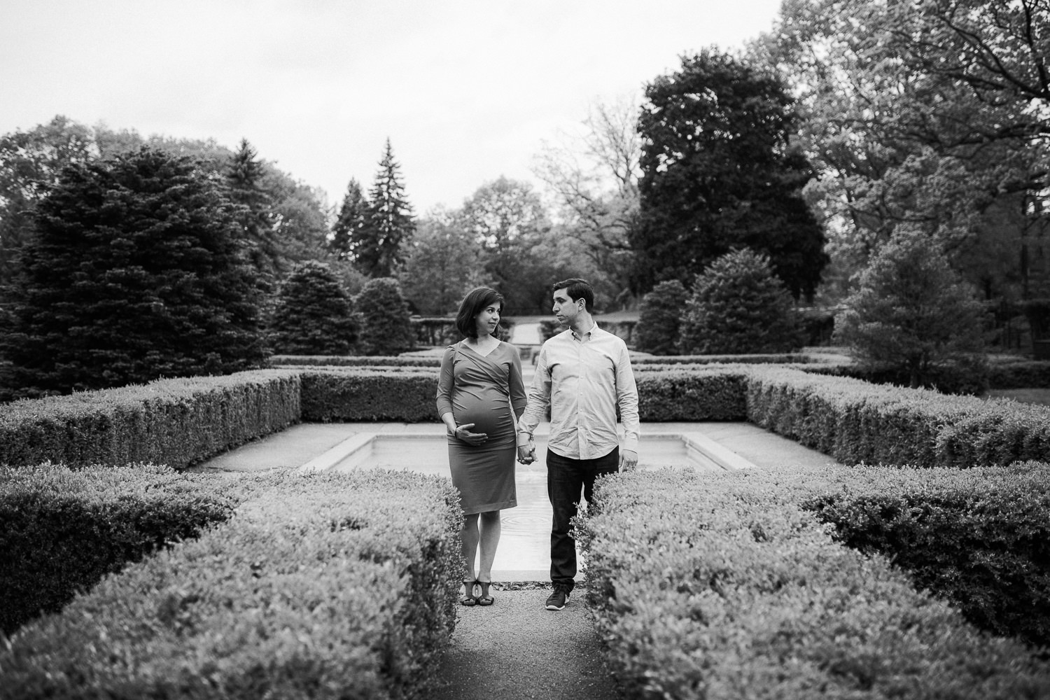 husband and pregnant wife stand holding hands and looking seriously at one another - Barrie Lifestyle Photography