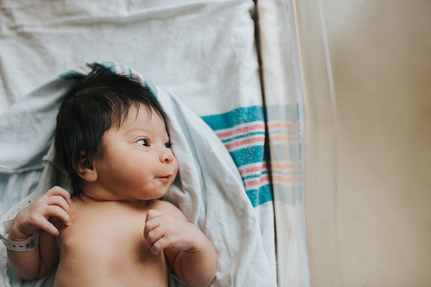 1 day old baby girl with lots of dark hair lying in hospital bassinet awake - Newmarket In-Hospital Photography 