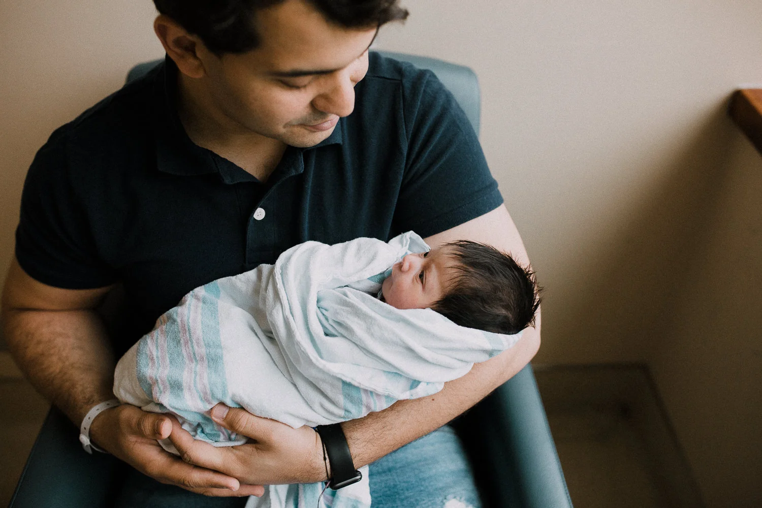 new dad sits in chair holding 1 day old baby girl swaddled in hospital blanket - Newmarket Fresh 48 Photos