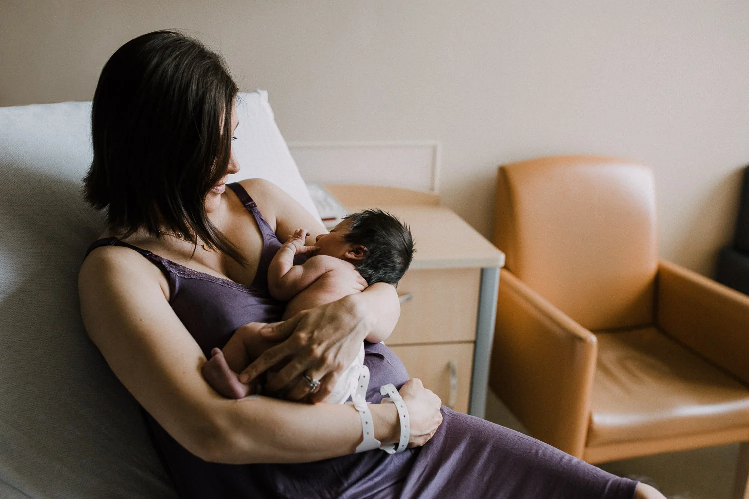 first time mom sitting on hospital bed holding 1 day old baby daughter - Markham In-Hospital Photos