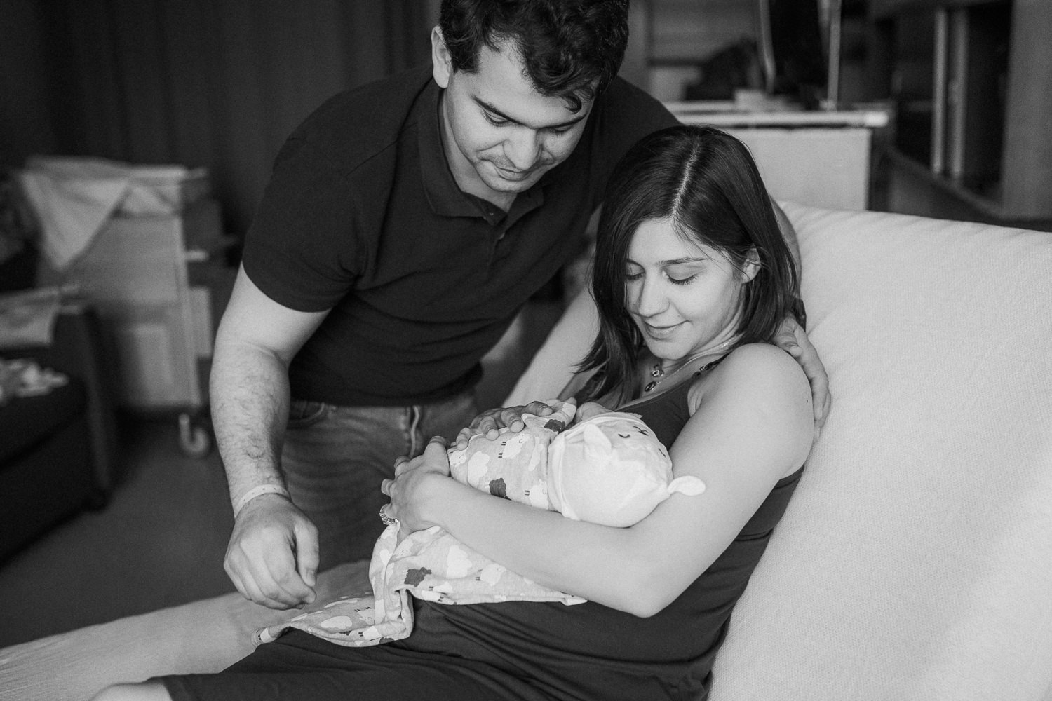 new mom sits on hospital bed holding 1 day old baby girl as dad leans over - Stouffville In-Hospital Photography