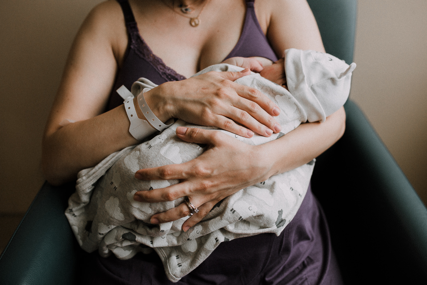 new mom sitting in chair holding 1 day old baby girl wrapped in swaddle - Newmarket Fresh 48 Photography