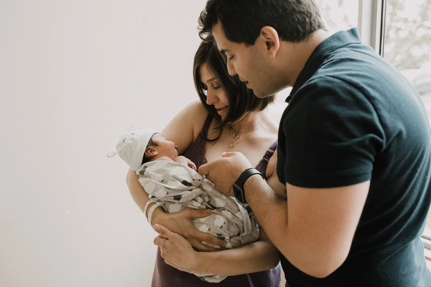 new family of 3 standing at window, parents holding and smiling at 1 day old baby daughter - Newmarket Fresh 48 Photos