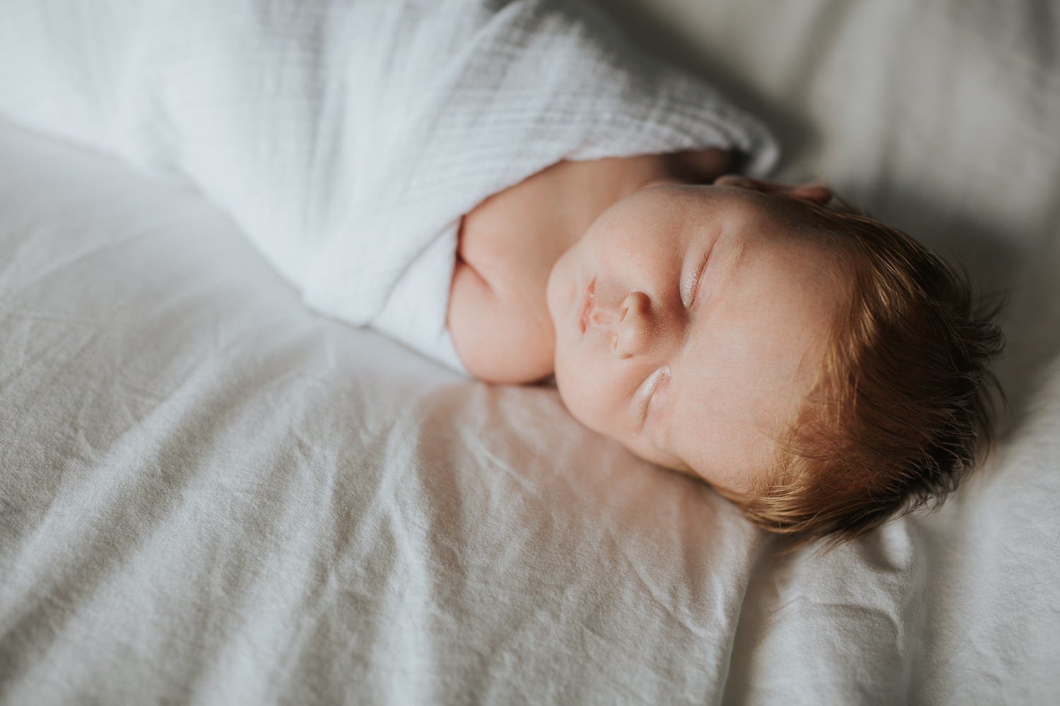 2 week old baby girl with red hair in white swaddle asleep on bed - Stouffville Lifestyle Photography