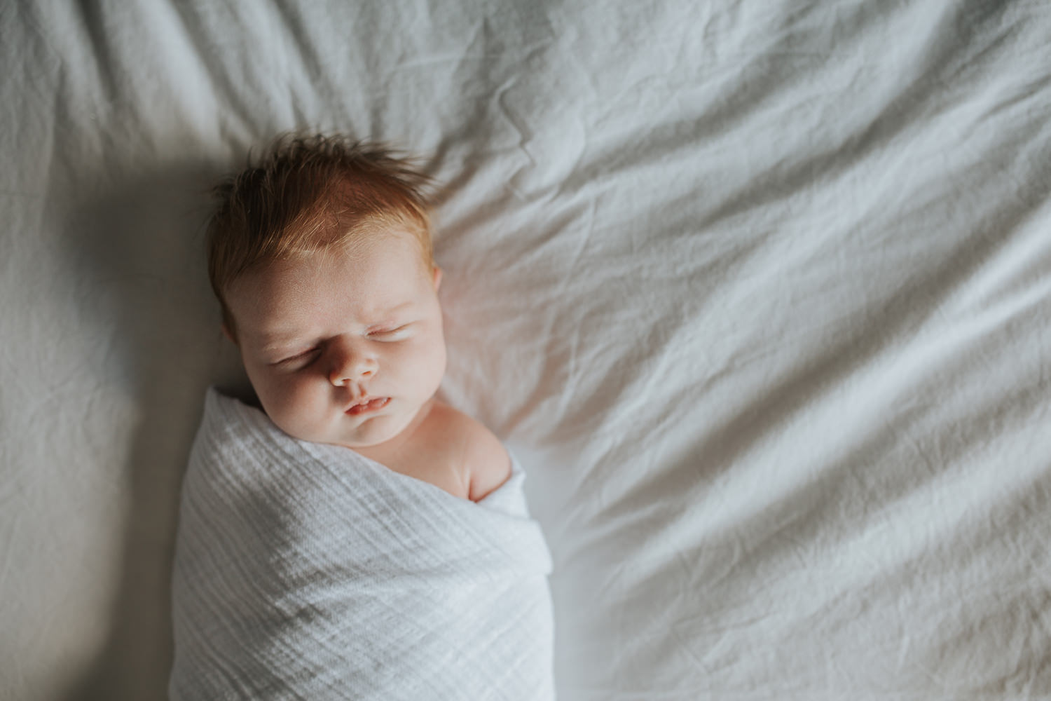 2 week old baby girl with red hair in white swaddle asleep on bed - Markham Lifestyle Photography