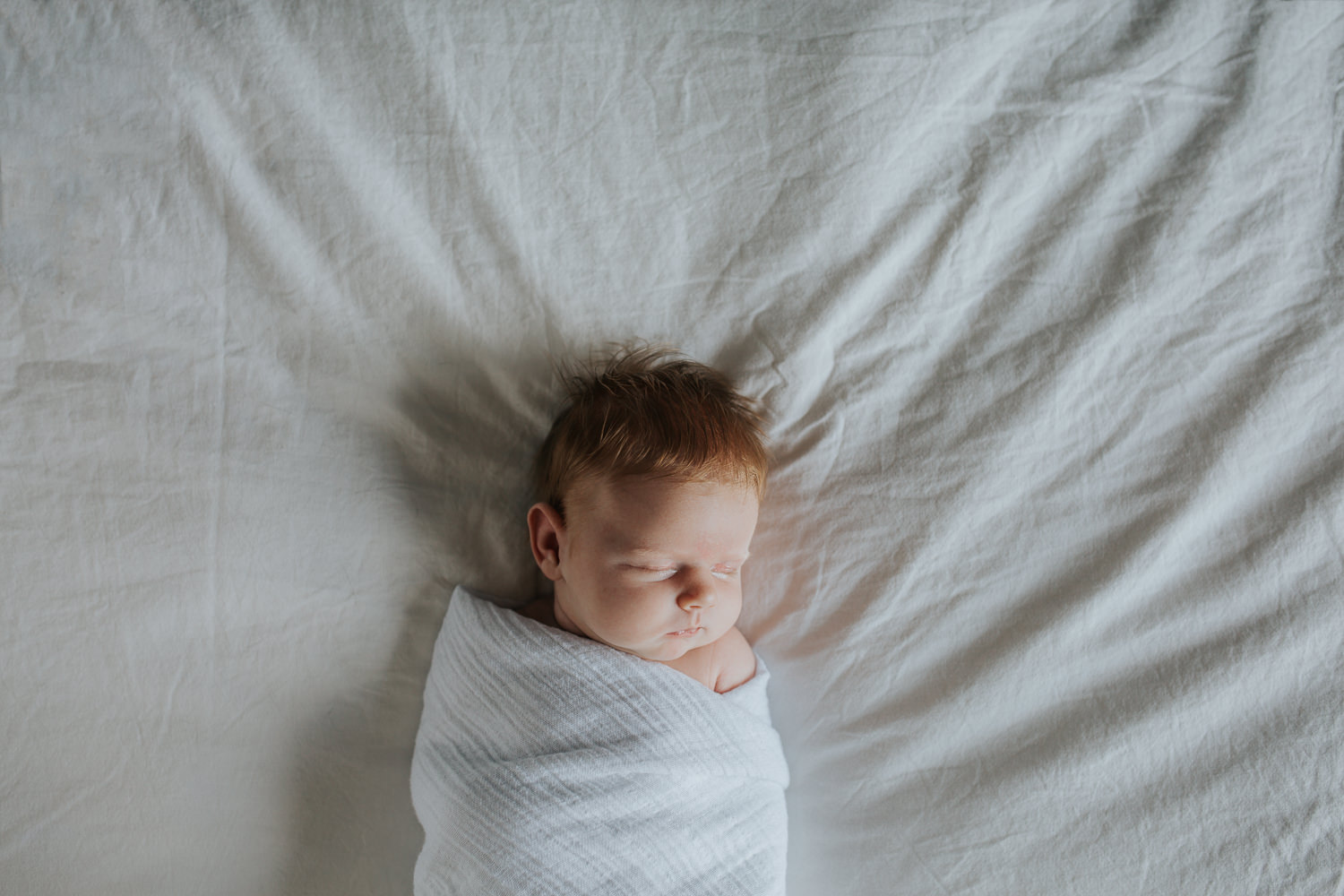 2 week old baby girl with red hair in white swaddle asleep on bed - Markham In-Home Photography