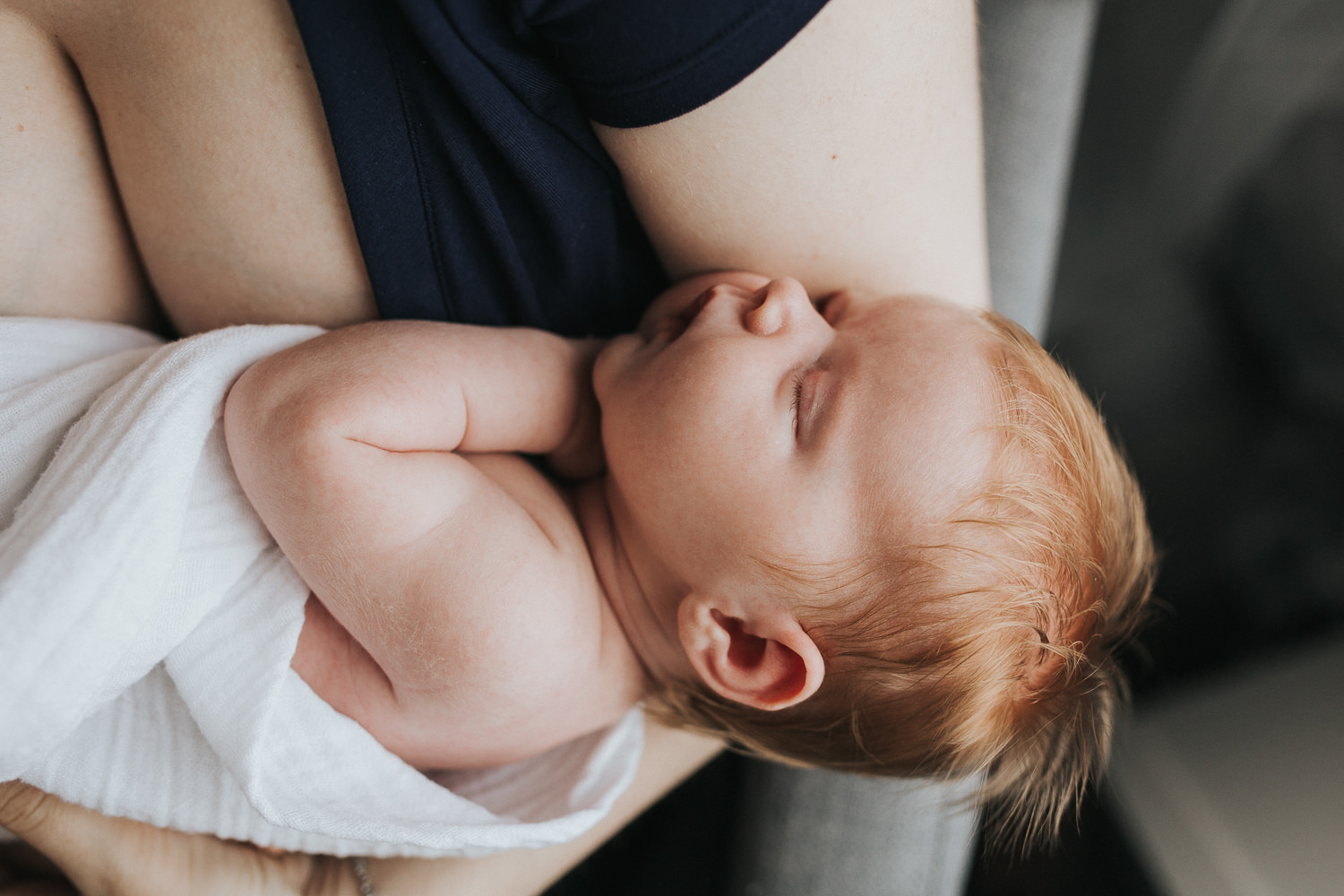 2 week old swaddled baby girl with red hair asleep in mother's arms - Barrie In-Home Photography