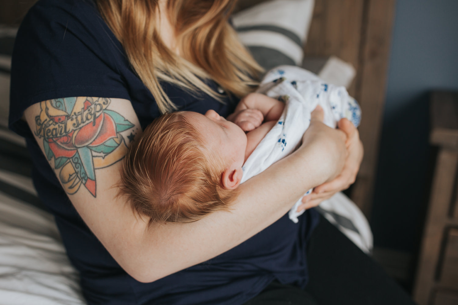 first time mom sitting on bed holding and looking at 2 week old baby girl with red hair - Newmarket In-Home Photography