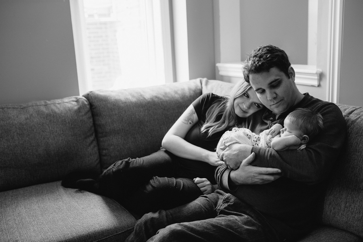 family of 3, new parents sitting on couch holding and looking at 2 week old baby girl - Barrie In-Home Photography