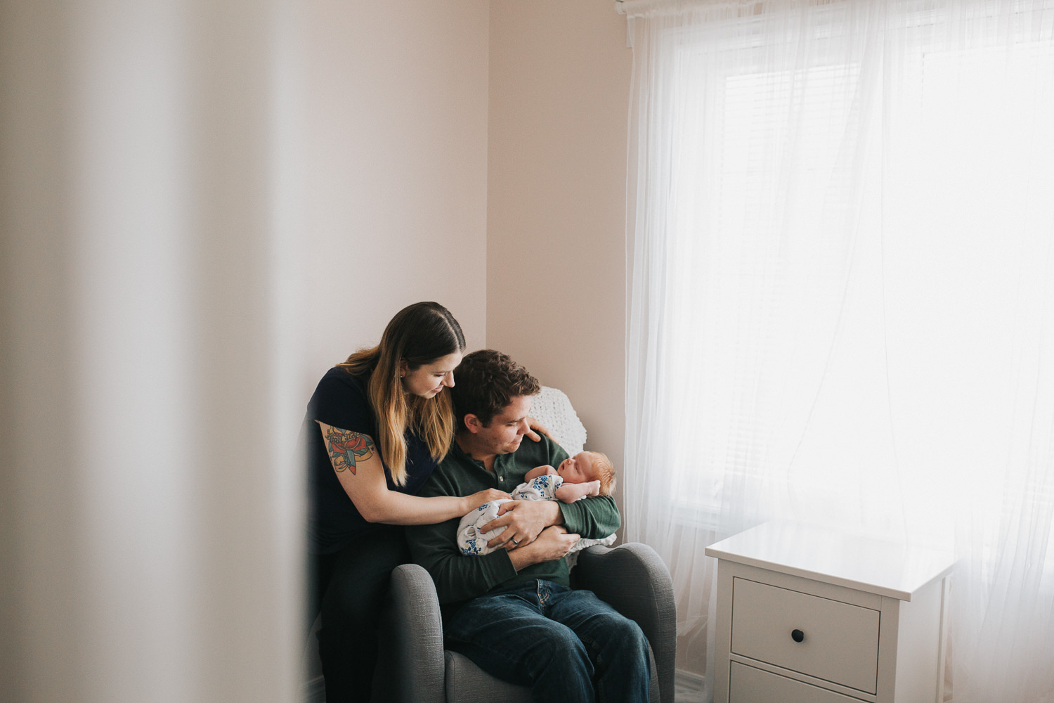 new parents sitting in nursery chair holding 2 week old baby girl with red hair - Stouffville In-Home Photos