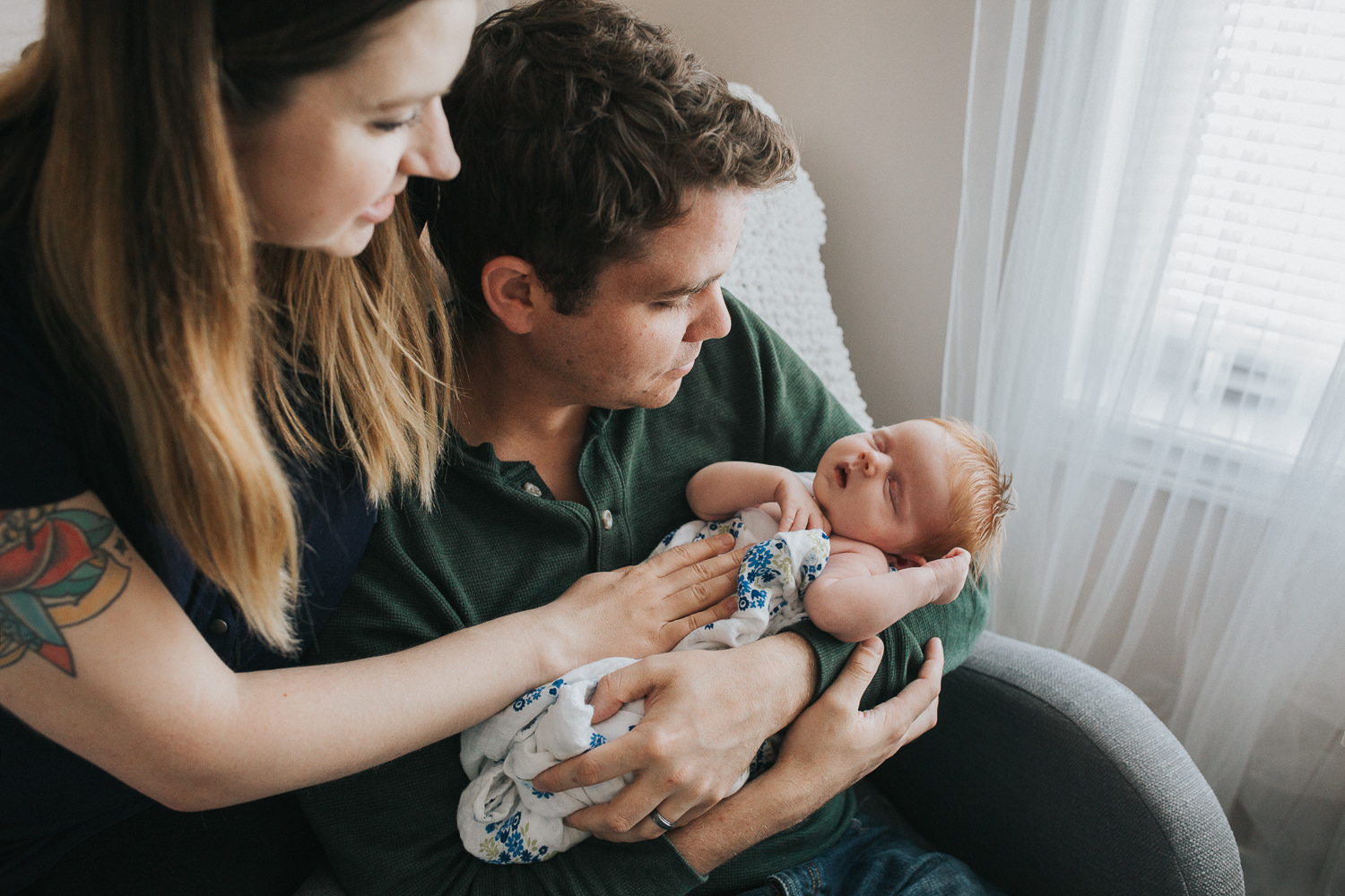 new parents sitting in nursery chair holding 2 week old baby girl with red hair - Barrie In-Home Photos