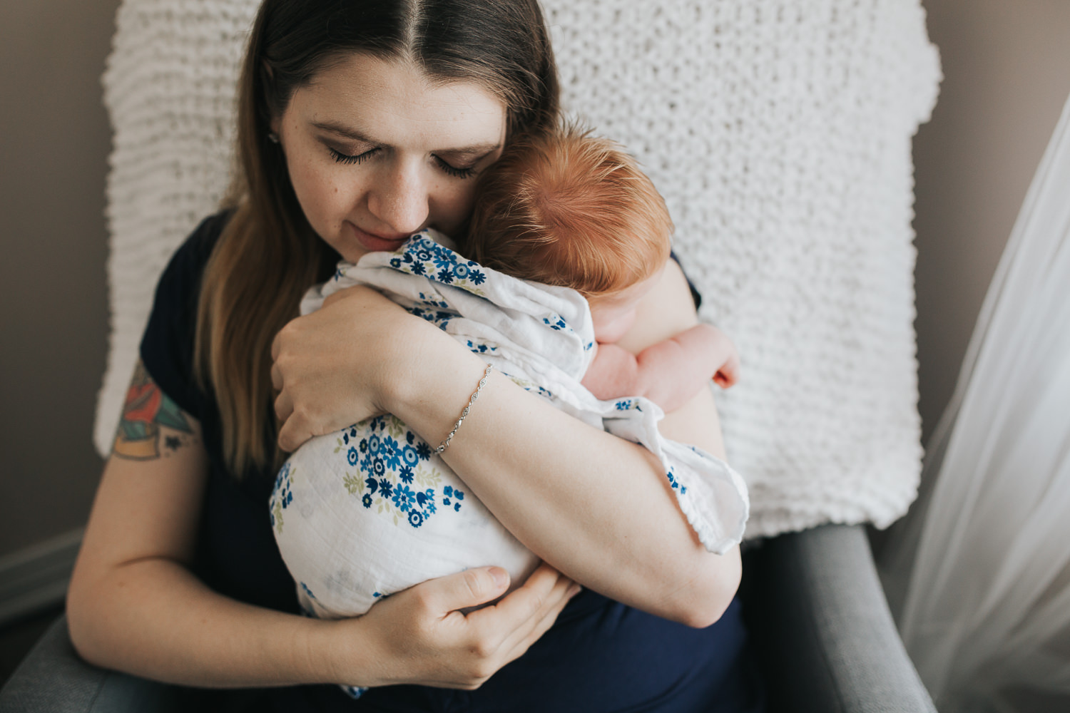 first time mom sitting in nursery chair holding sleeping 2 week old baby girl with red hair - Markham Lifestyle Photos