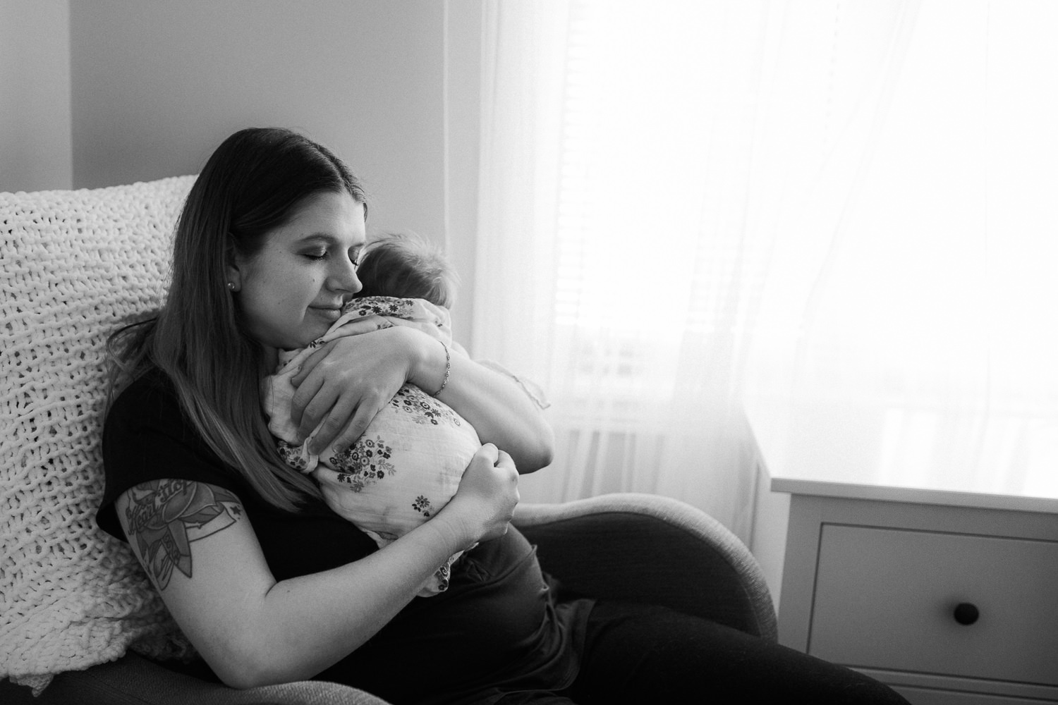 first time mom sitting in nursery chair holding sleeping 2 week old baby girl with red hair - Barrie Lifestyle Photos