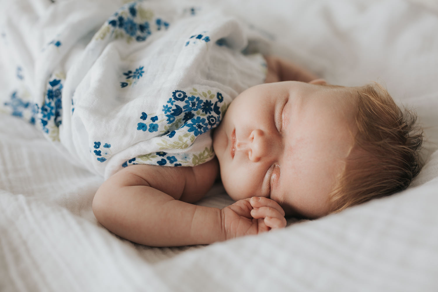 2 week old baby girl with red hair asleep on bed wrapped in blue floral swaddle - Stouffville Lifestyle Photography