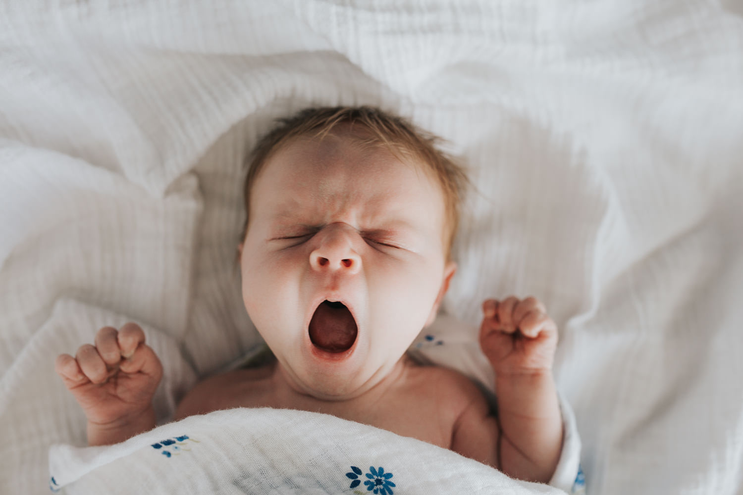 2 week old baby girl with red hair yawning on bed wrapped in blue floral swaddle - Newmarket In-Home Photography