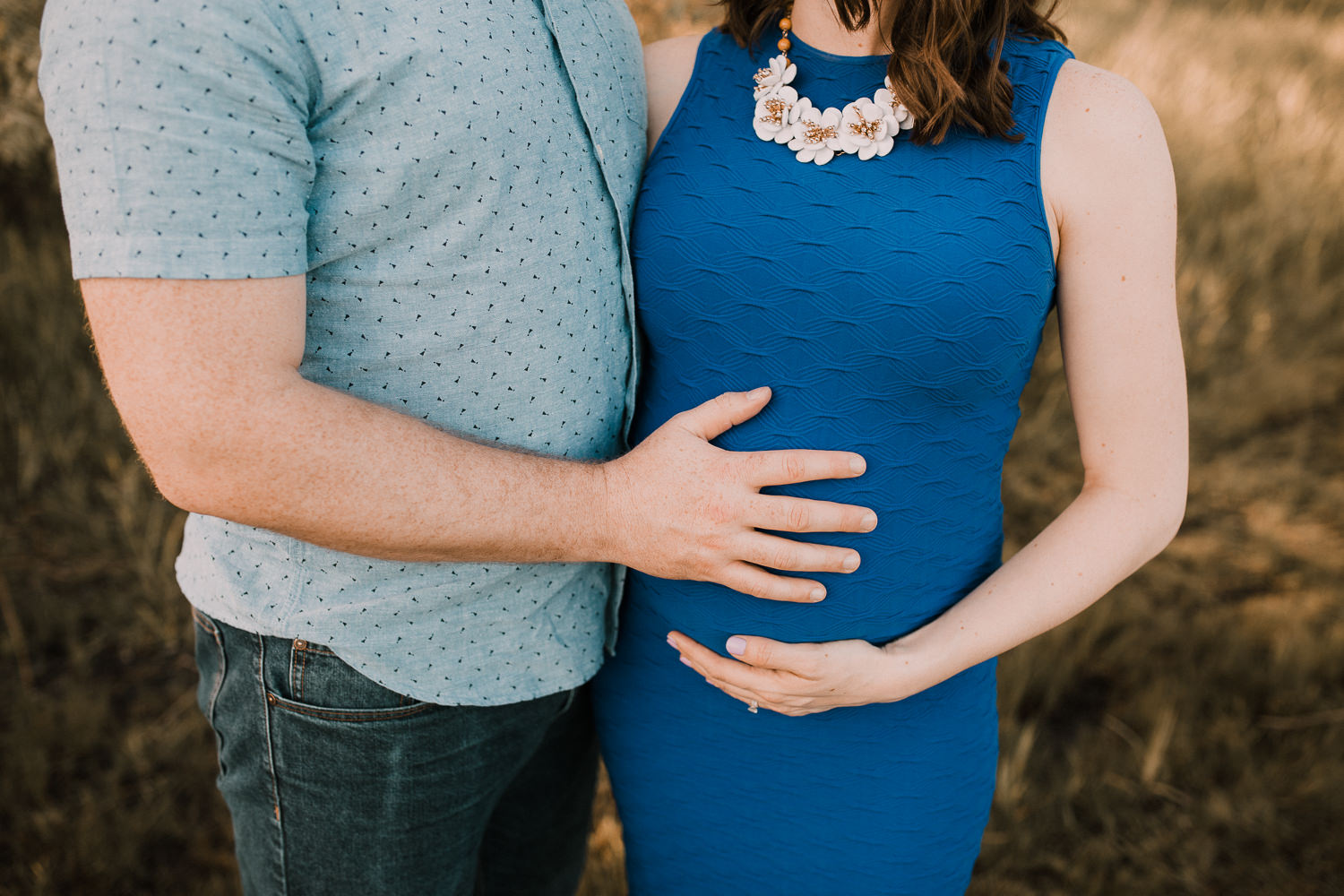 husband with pregnant brunette wife in blue dress while with hands on baby bump - Markham Lifestyle Photography