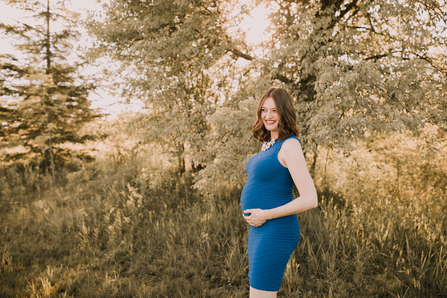 pregnant brunette mom-to-be stands holding baby bump at sunset - Markham Lifestyle Photos
