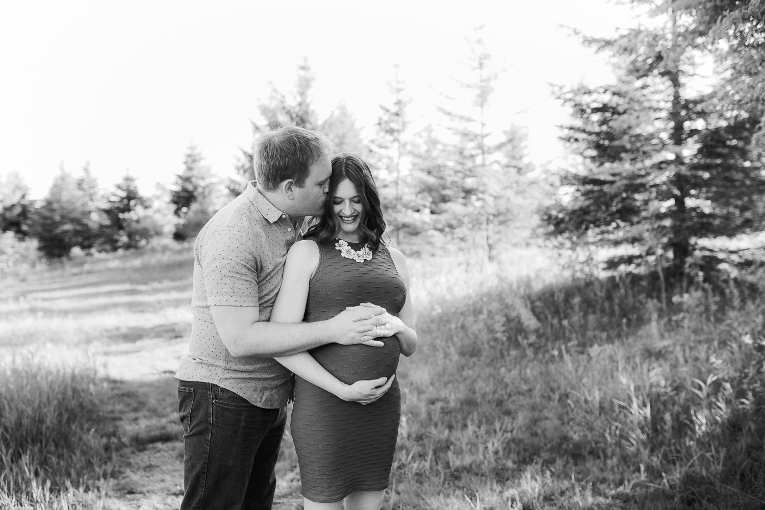 husband embraces pregnant wife and kisses her on cheek at sunset - Stouffville Outdoor Photography