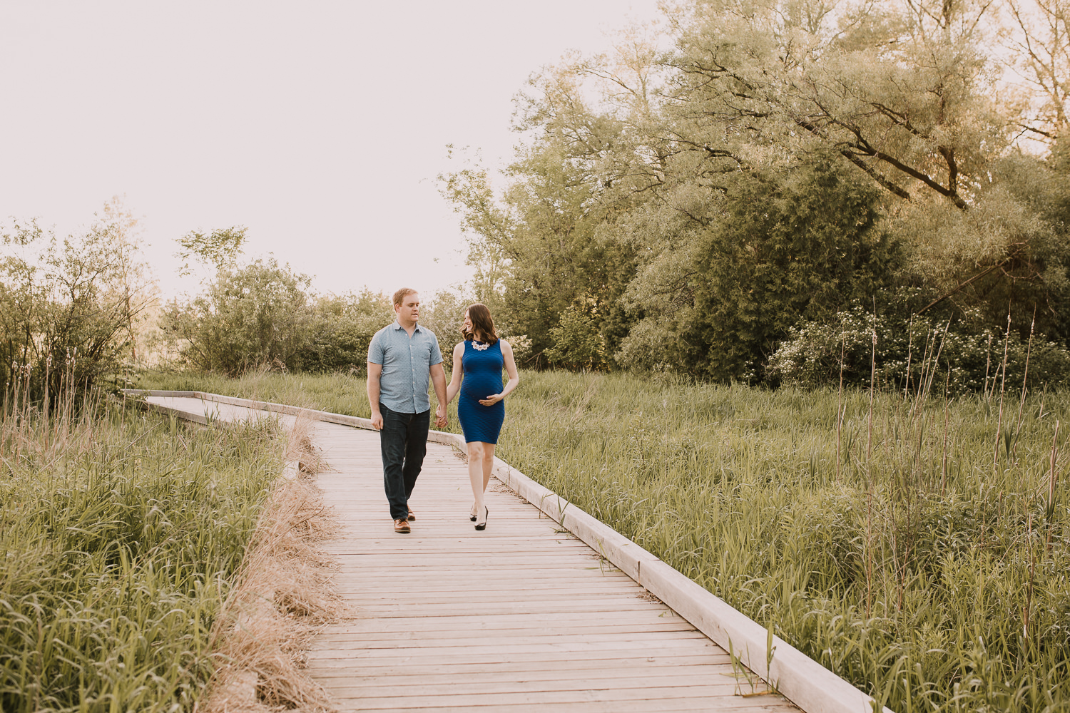 pregnant brunette mom-to-be holds husband's hand as they walk along bridge - Markham Outdoor Photography