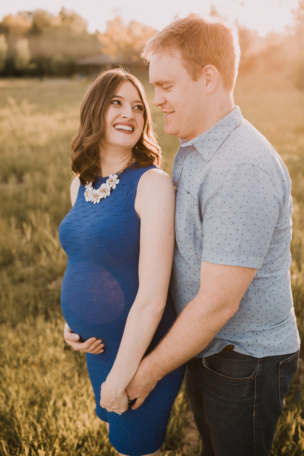 pregnant brunette mom-to-be in blue dress holding husband's hand and smiling at him - Stouffville Lifestyle Photos