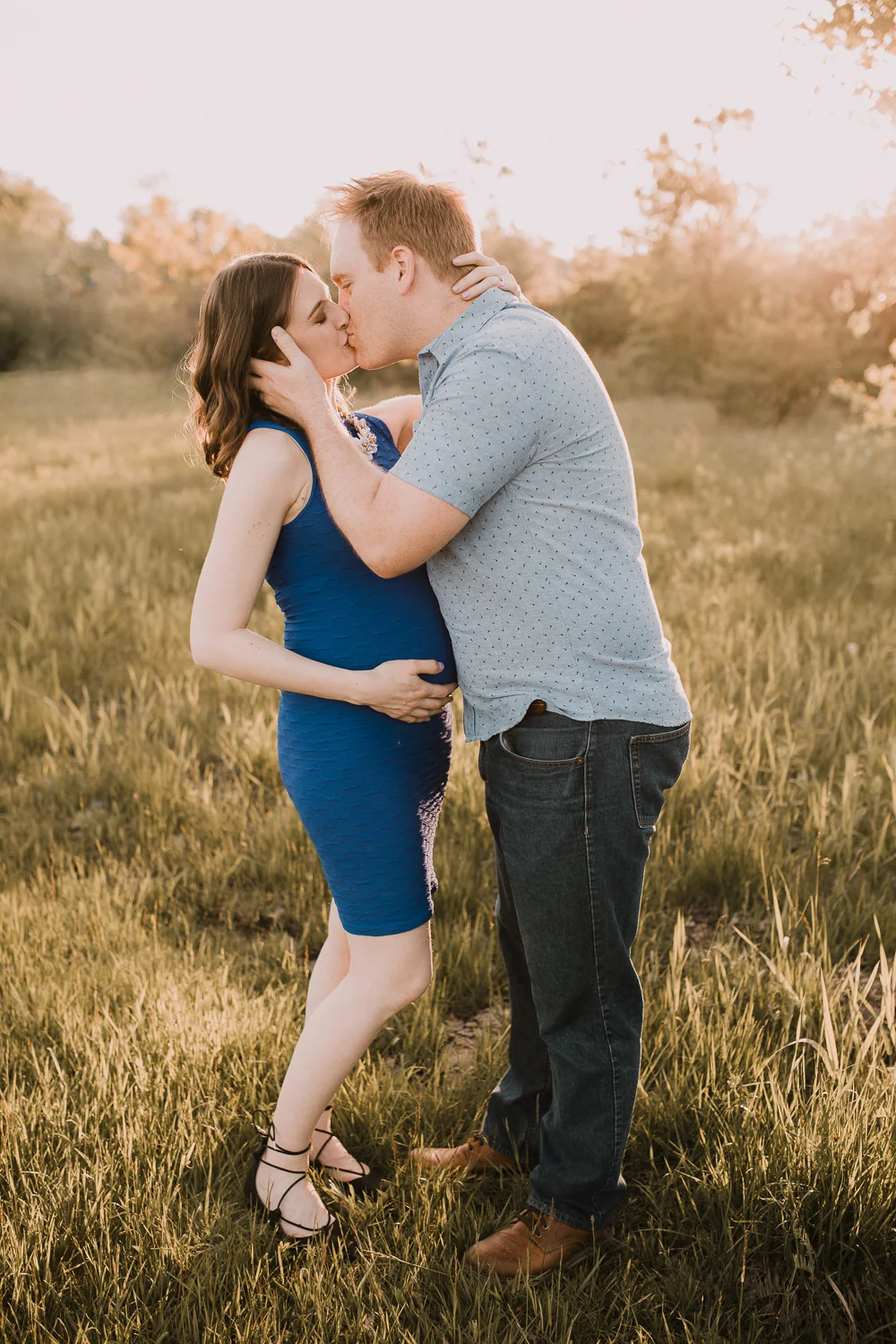 father-to-be kissing pregnant brunette wife in golden field at sunset - Markham Lifestyle Photos