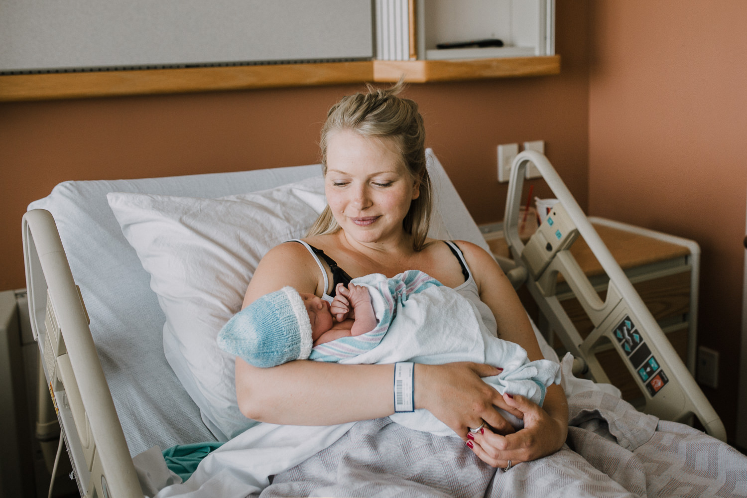 first time mom sitting in hospital bed holding 10 hour old baby boy - Barrie Fresh 48 Photography