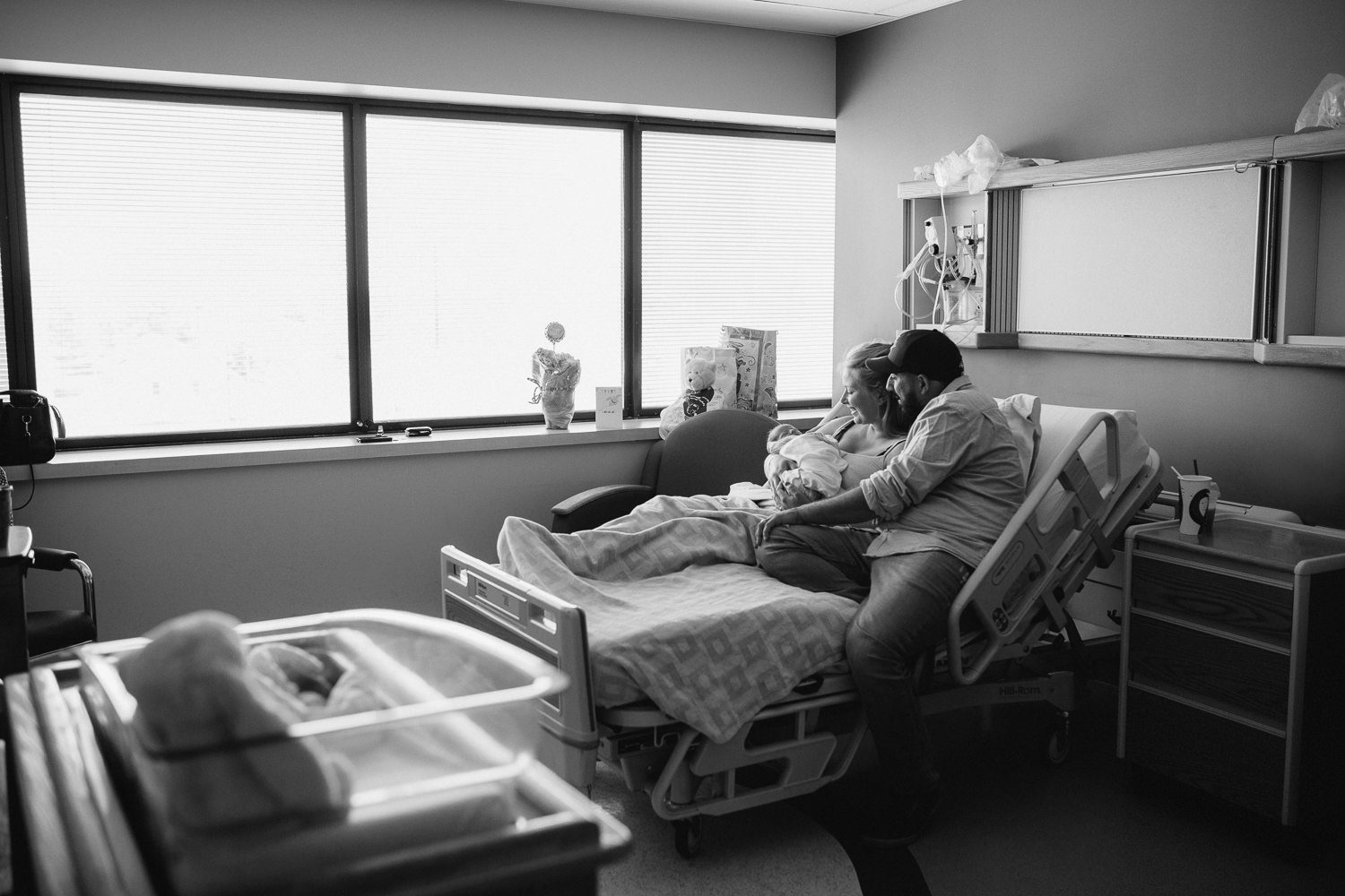 brand new parents sitting in hospital bed holding and looking at 10 hour old baby boy - Markham In-Hospital Photos