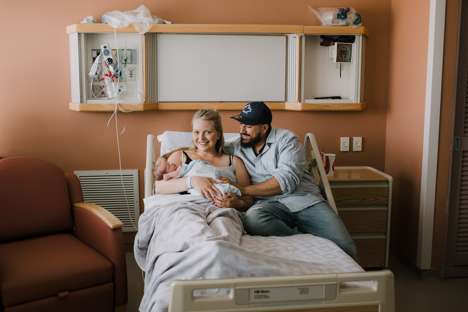 first time parents sitting in hospital bed holding and looking at 10 hour old baby boy - Stouffville In-Hospital Photography