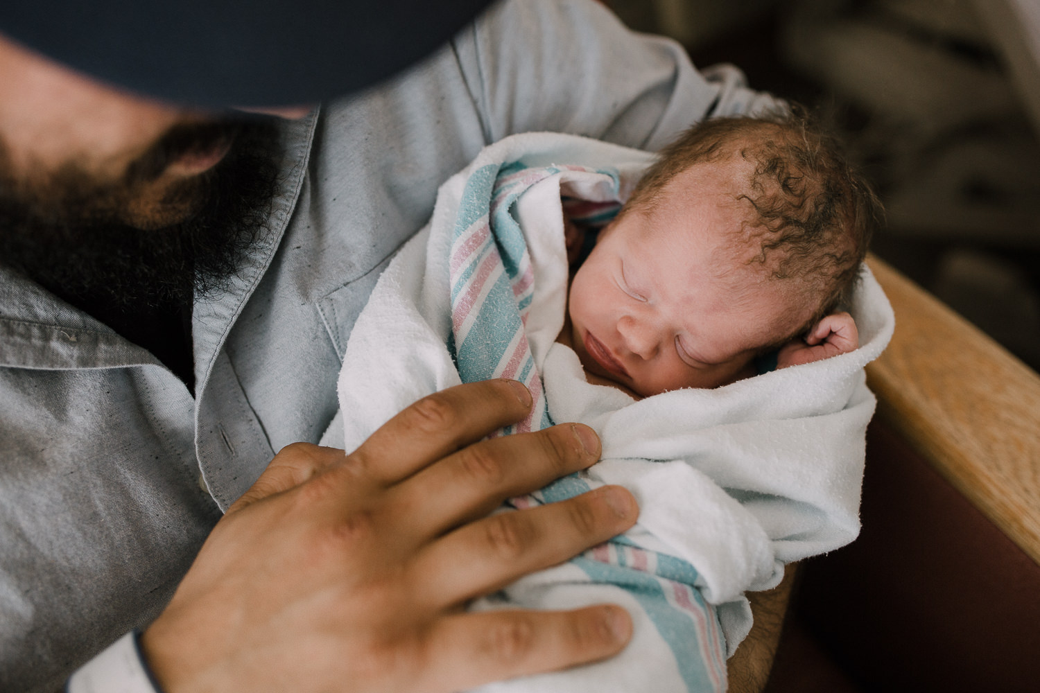 new dad sitting in hospital chair holding swaddled, sleeping 10 hour old baby boy -​​​​​​​ Stouffville In-Hospital Photography