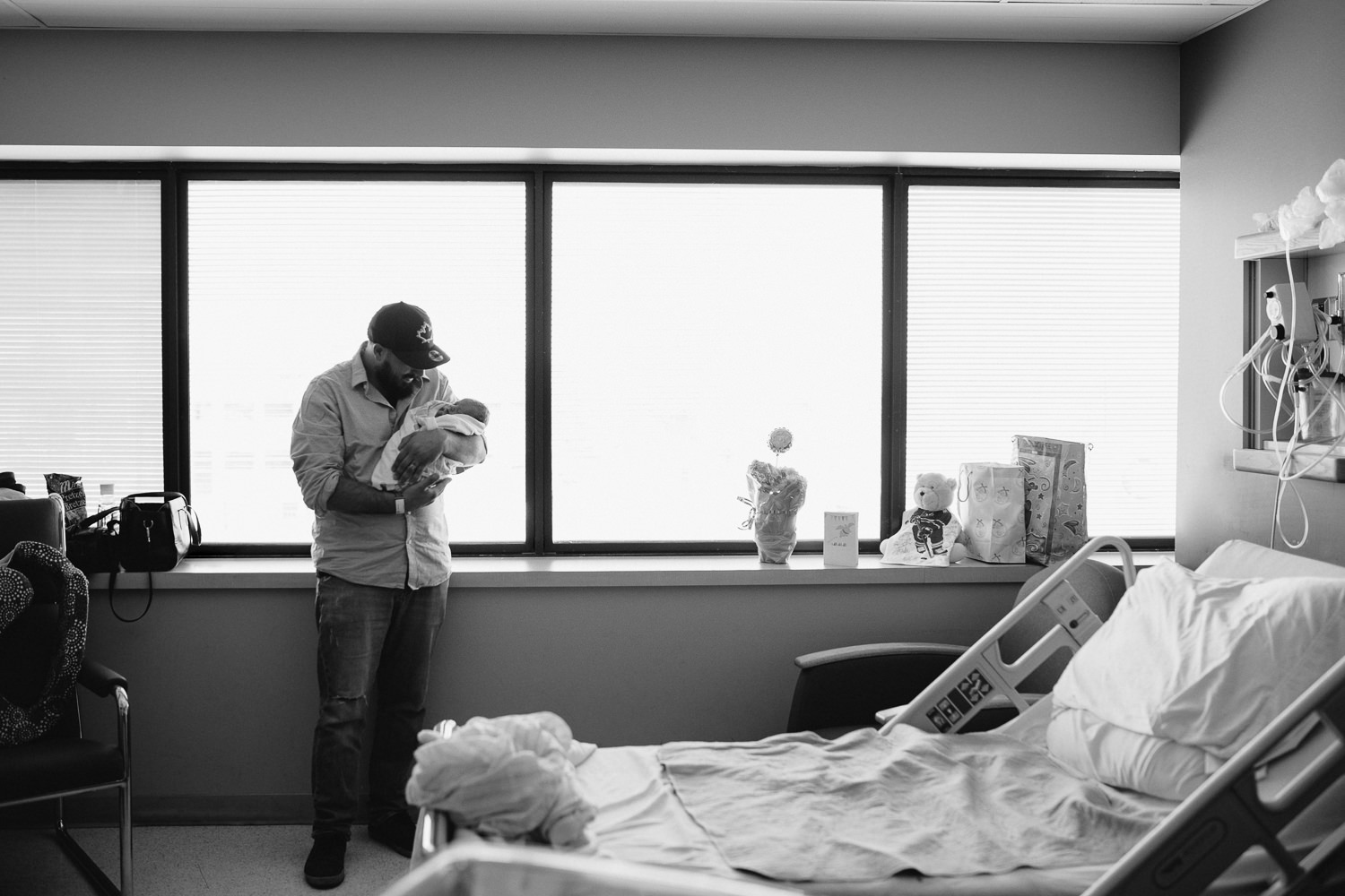 new dad standing in hospital room holding swaddled, sleeping 10 hour old baby boy -​​​​​​​ Barrie In-Hospital Photography