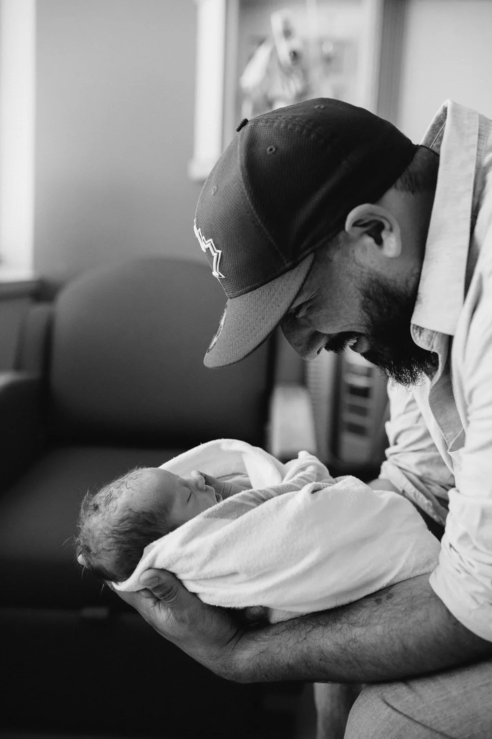 new father sitting on hospital bed smiling at swaddled, sleeping 10 hour old baby boy - Newmarket Fresh 48 Photography