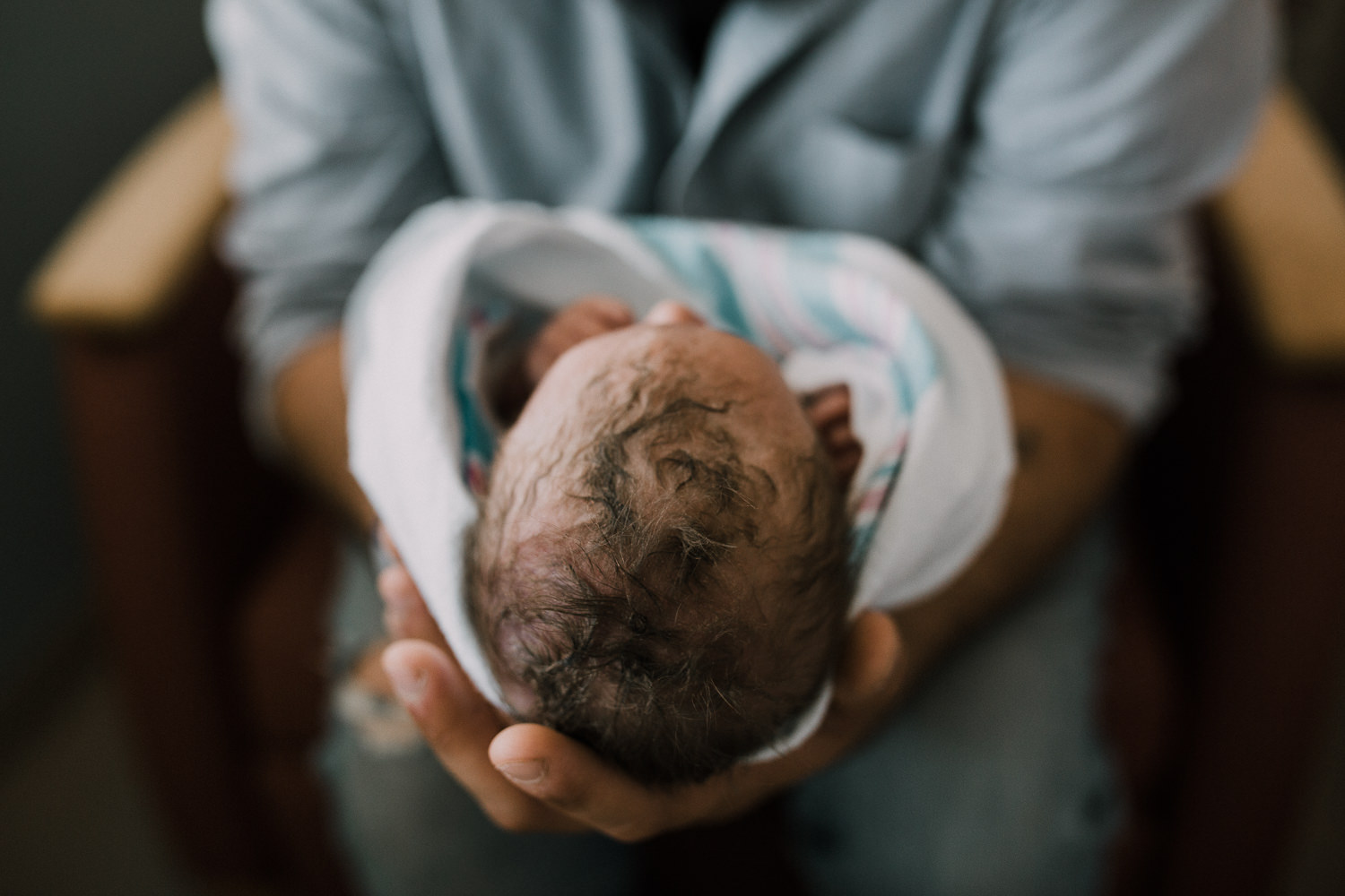 new dad sitting in hospital chair holding swaddled, sleeping 10 hour old baby boy, close up of baby's hair -​​​​​​​ Barrie Fresh 48 Photography