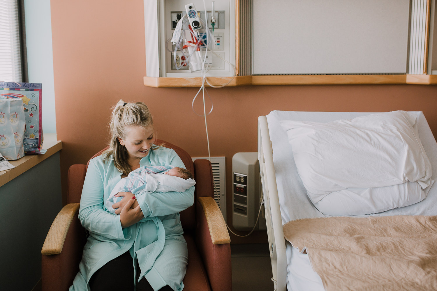 new mother sitting in hospital chair holding swaddled 10 hour old baby boy -​​​​​​​ Barrie In-Hospital Photos