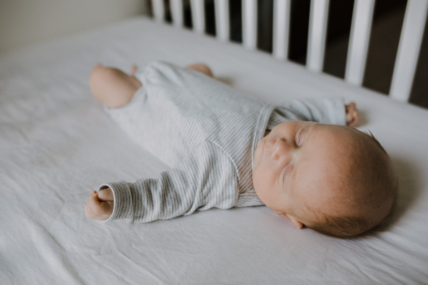 2 week old baby boy in grey onesie sleeping in nursery crib - Markham Lifestyle Photography