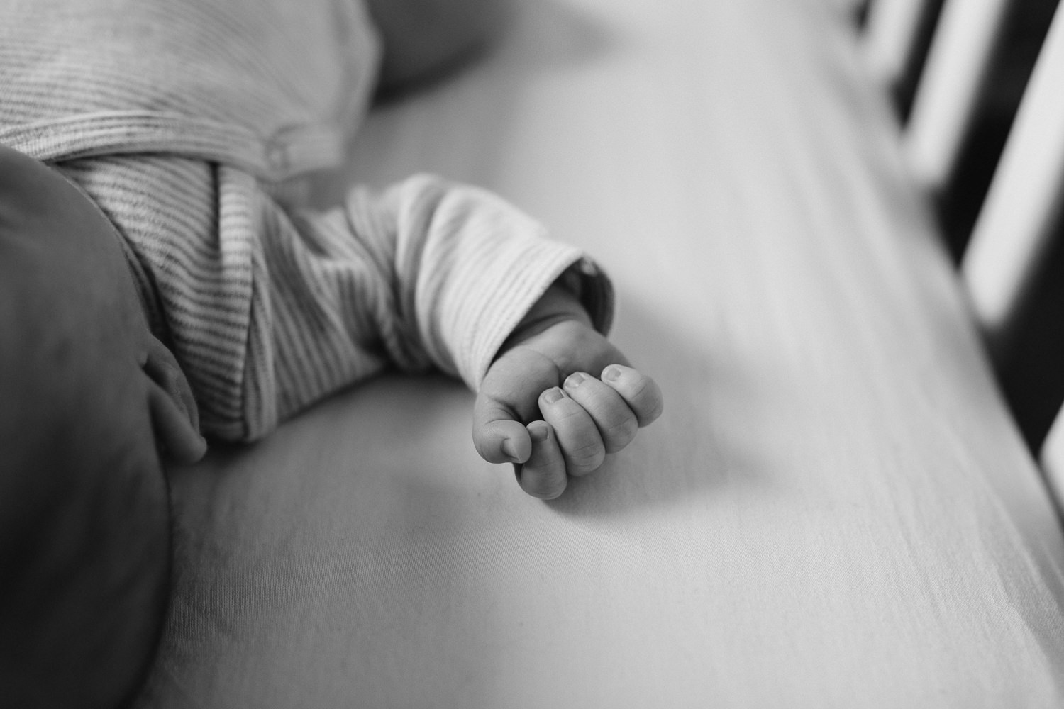 2 week old baby boy in grey onesie sleeping in nursery crib, closeup of hand - Stouffville In-Home Photography