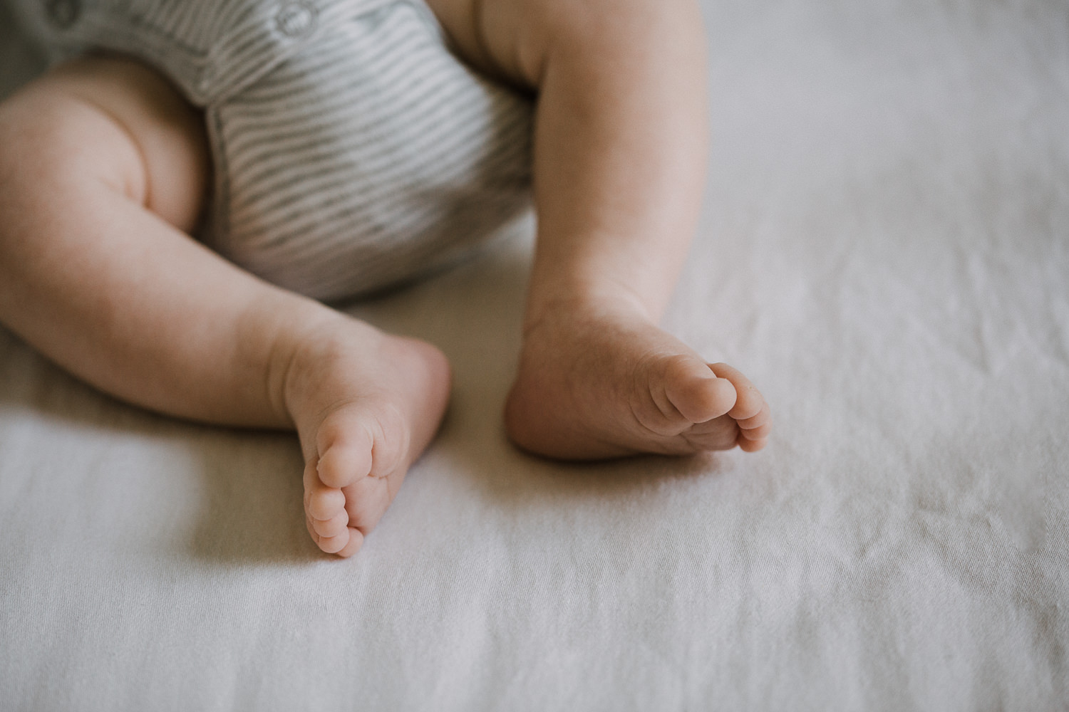 2 week old baby boy in grey onesie sleeping in nursery crib, close up of feet - Markham In-Home Photography